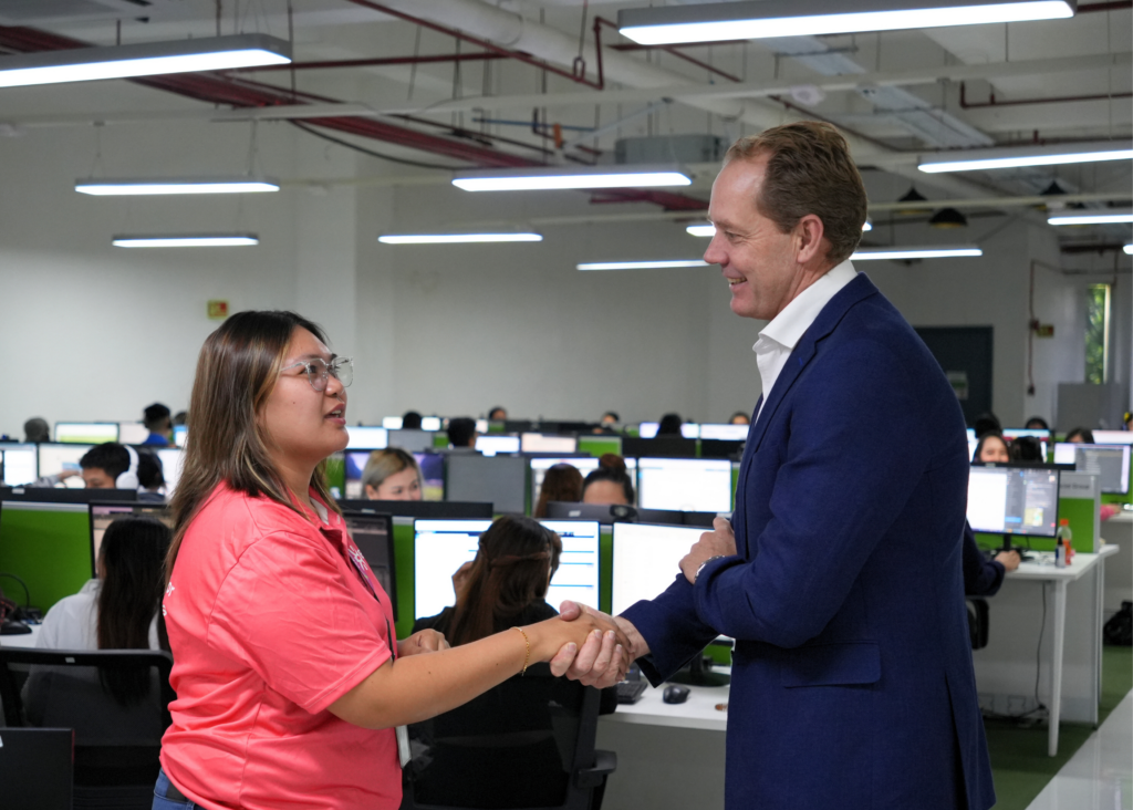 Team member shaking hands with CEO at the office, at the background are team members working in the office