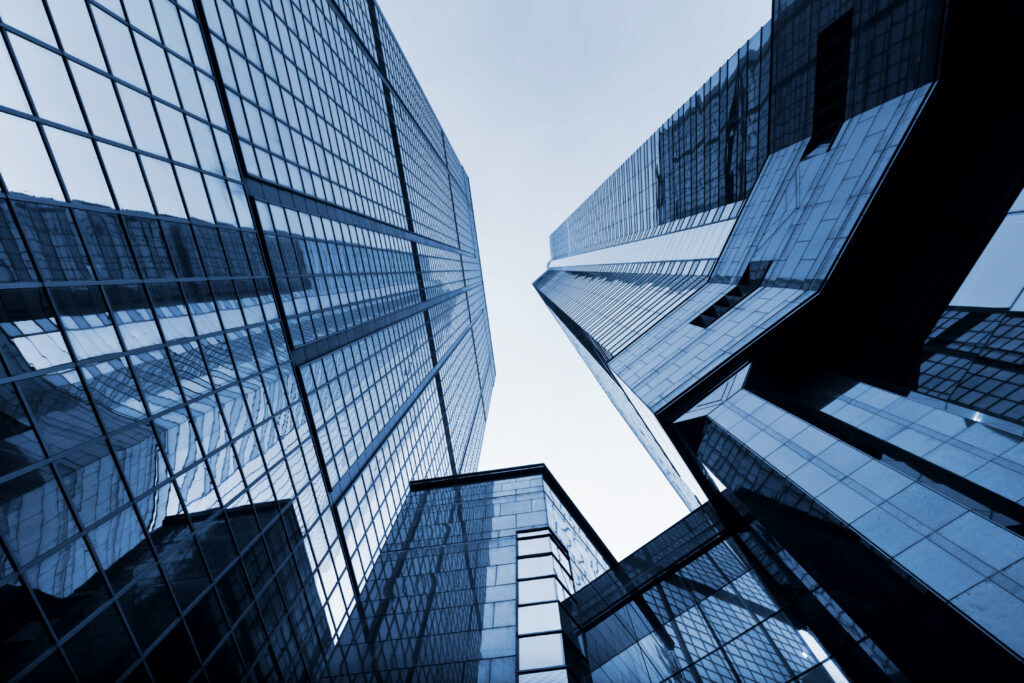 Upward view of blue-toned skyscrapers with glass facades reflecting the sky — symbolising growth and ambition.